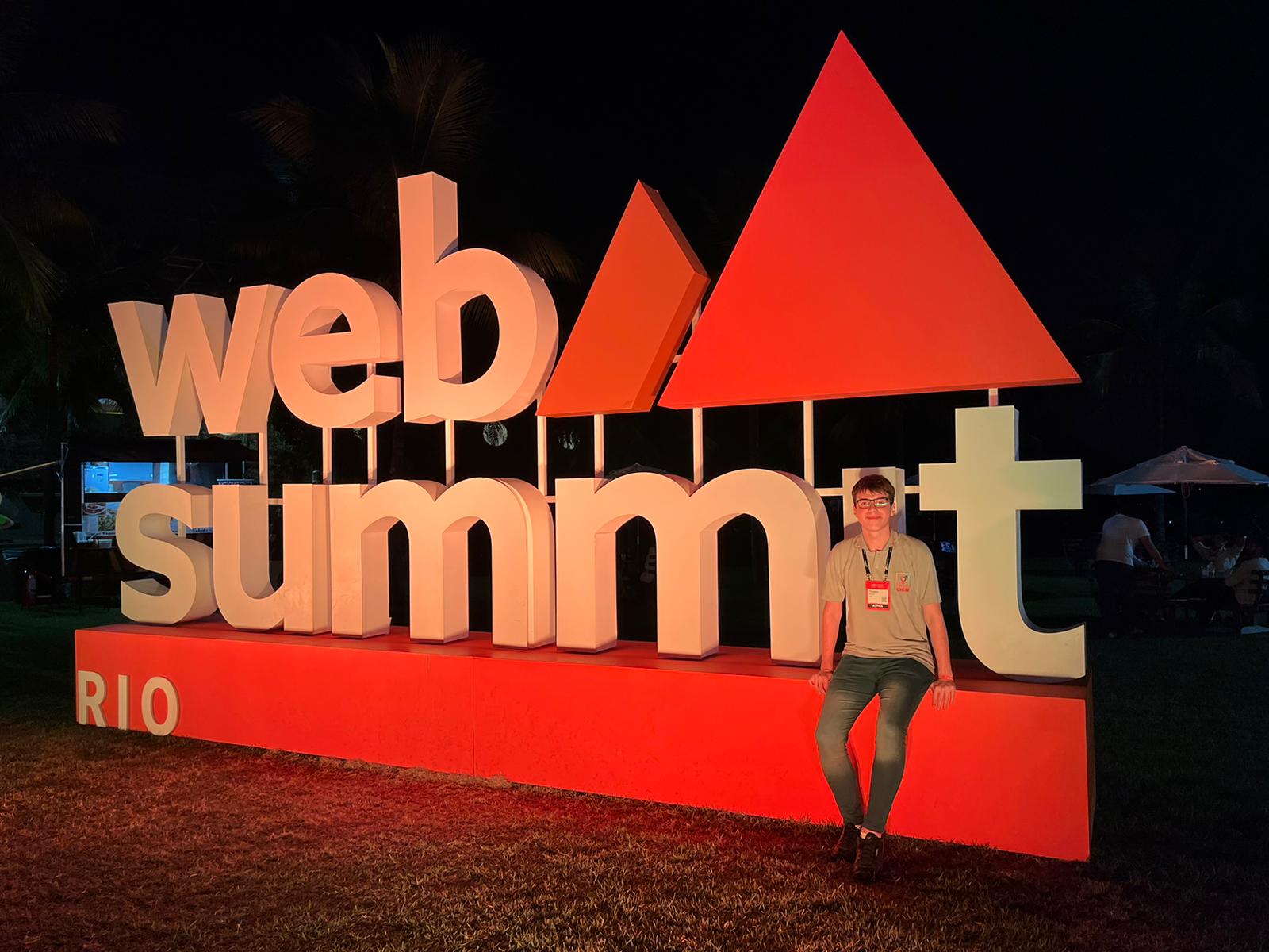 Ticiano sitting on the sign of Web Summit Rio 2023